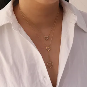 Detail view of double-layered gold heart tassel necklace worn on a white shirt