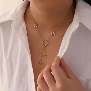 Macro detail of a minimalist gold-plated heart tassel necklace worn with a white shirt