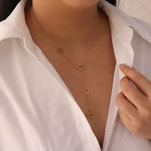 Detail of gold stainless steel heart tassel necklace on model wearing white shirt.