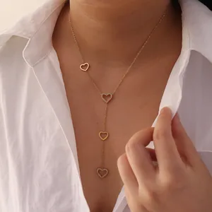 Detailed close-up of an elegant gold heart tassel necklace worn over a white shirt