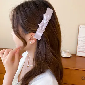 Detailed view of a Korean-style satin bow hair clip with rhinestones on a model.