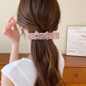 Elegant satin ribbon bow hair clip with sparkling rhinestones worn on long brown wavy hair.