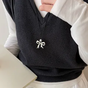 Detailopname van een zilveren strikhanger aan een minimalistische zwarte koordketting.