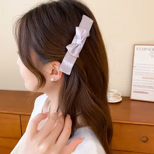 Detail of a light purple satin bow hair clip with rhinestones worn on a woman's side hair.