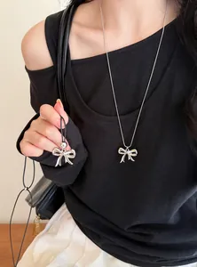 Detail van een minimalistische zilveren strik hanger ketting op een zwarte top met mouwen