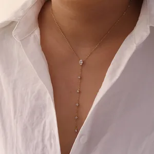 Close-up of a gold Y-shaped drop necklace with white crystals on a white shirt model