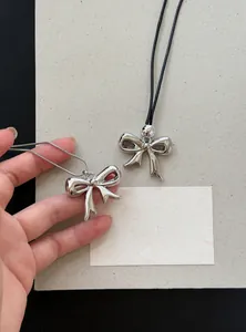 Detail van zilveren strik hanger ketting met slangenketting en zwart leren koord
