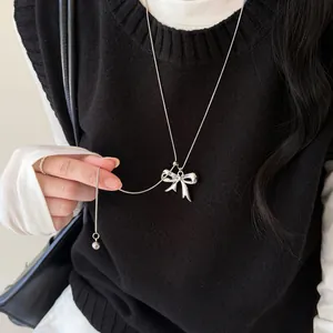 Close-up detail van een elegante zilveren strikhanger ketting gedragen op een zwart vest