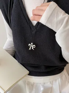 Detail van zilveren strikhanger aan zwart koord met minimalistische kleding.