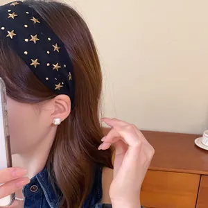 Detalle de una diadema ancha de tela negra con tachuelas de estrellas doradas.