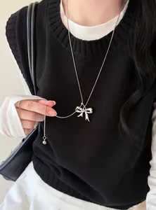 Detailopname van een zilveren ketting met strikhanger gedragen over een zwarte gebreide top