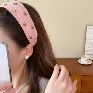 Primer plano de una diadema ancha de tela rosa decorada con tachuelas de estrellas doradas