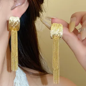 Close-up of gold earrings featuring a unique wrinkled texture and long chain tassels.