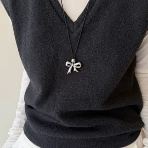 Detailopname van een zilveren strikhanger aan een zwarte leren koordketting op een vest