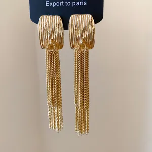 Close-up detail of gold square crinkle stud earrings with long layered chain tassels.