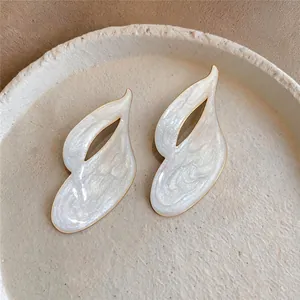 Close-up detail of minimalist flame-shaped white pearlescent enamel earrings with gold metal trim