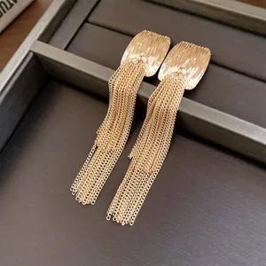 Close-up of gold French style wrinkled square stud earrings with long chain tassels