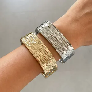 Detail van goud- en zilverkleurige metalen armbanden met unieke geplooide patronen.