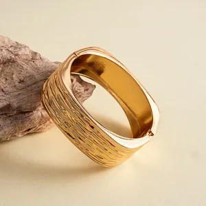 Detail van gouden vierkante armband met een opvallende textuur en glanzende afwerking.