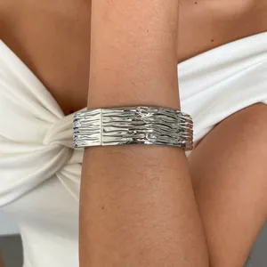 Close-up van een zilverkleurige geometrische armband met crinkle-structuur om de pols