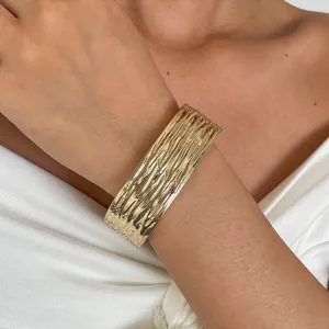 Detailweergave van een gouden manchetarmband met elegante gehamerde verticale plooien.