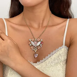 Detail van een vintage gouden engel hanger ketting met roze bloemen en hartvormig kristal