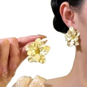 Eleganti orecchini a lobo a fiore dorati indossati all'orecchio e in mano