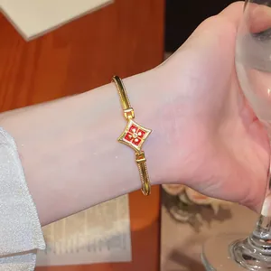 Détail d'un bracelet élégant plaqué or avec motif fleur rouge porté au poignet.