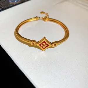 Détail d'un bracelet plaqué or 24K avec motif floral en émail rouge et pierre de zircon.