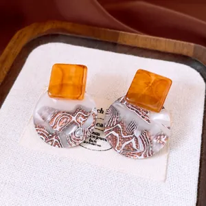 Close-up of retro resin geometric earrings with amber square and marble circle pattern.