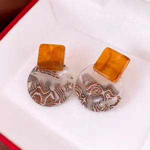 Macro detail of vintage resin earrings with amber square and patterned round pendants.