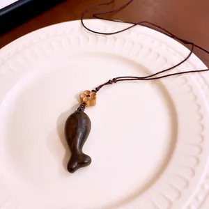 Minimalistische Holzkette mit Fisch-Anhänger im Retro-Stil auf einem weißen Porzellanteller