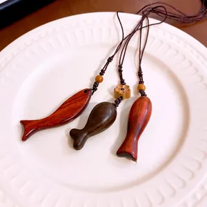 Handgefertigte Retro-Halsketten mit Fischanhänger aus Holz auf weißem Dekoteller
