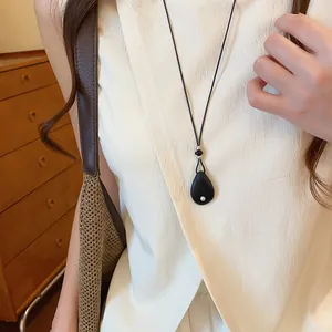 Retro ketting met druppelhanger aan een zwart leren koord gedragen op witte kleding