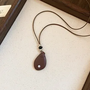 Gedetailleerd overzicht van een retro druppelhanger ketting aan een bruin leren koord.