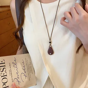 Detailweergave van een retro ketting met druppelvormige hanger en bruin lederen koord.