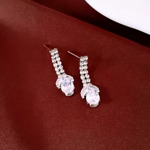 Eleganti orecchini a goccia in zircone argento su un lussuoso tessuto di raso rosso scuro