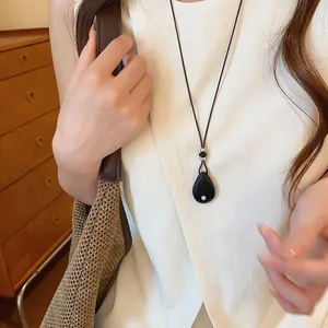 Detailopname van een minimalistische ketting met zwarte druppelhanger en leren koord.