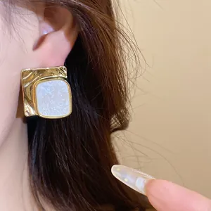 Close-up of golden square earrings with pleated texture and white marbled inlay on ear