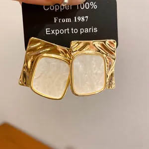 Macro detail of fashionable gold wrinkled square stud earrings with white pearlescent inlay