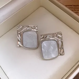 Close-up detail of silver-toned wrinkled square stud earrings with marble texture