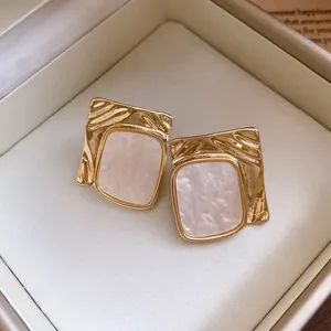 Close-up of elegant square pleated gold earrings with marbled resin inlay