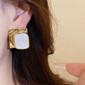 Macro detail of gold textured square stud earrings with white marbled resin inlay.