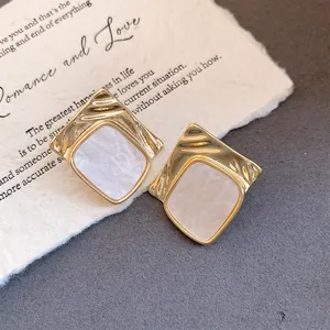 Detailed macro view of elegant gold wrinkled square stud earrings with white marble inlay texture