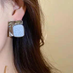 Close-up of silver textured square stud earrings with white acetate inlay on ear