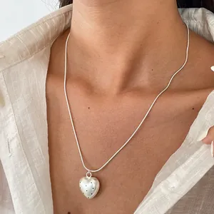 Primo piano di una collana con pendente a cuore a pois su una catena a serpente in argento