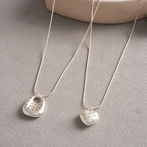 Dettaglio di collane geometriche minimaliste a cuore e ovali in tonalità argento