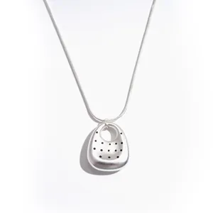 Collana minimalista con pendente ovale traforato color argento e pois neri su sfondo bianco