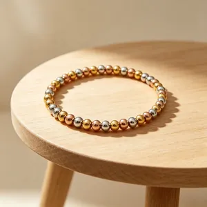 Detail eines dreifarbigen, 18 Karat vergoldeten Edelstahl-Perlenarmbands auf Holz.