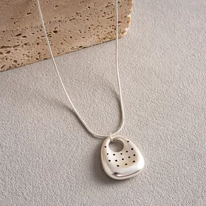 Dettaglio di una collana d'argento con un pendente traforato a pois dal design unico.